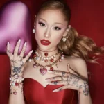 Ariana Grande reclining in red satin with layered Swarovski heart necklaces and pearl earrings