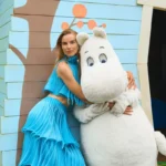Suvi Riggs Koponen posing with the Moomin outside a pastel-blue cottage for Vogue Scandinavia